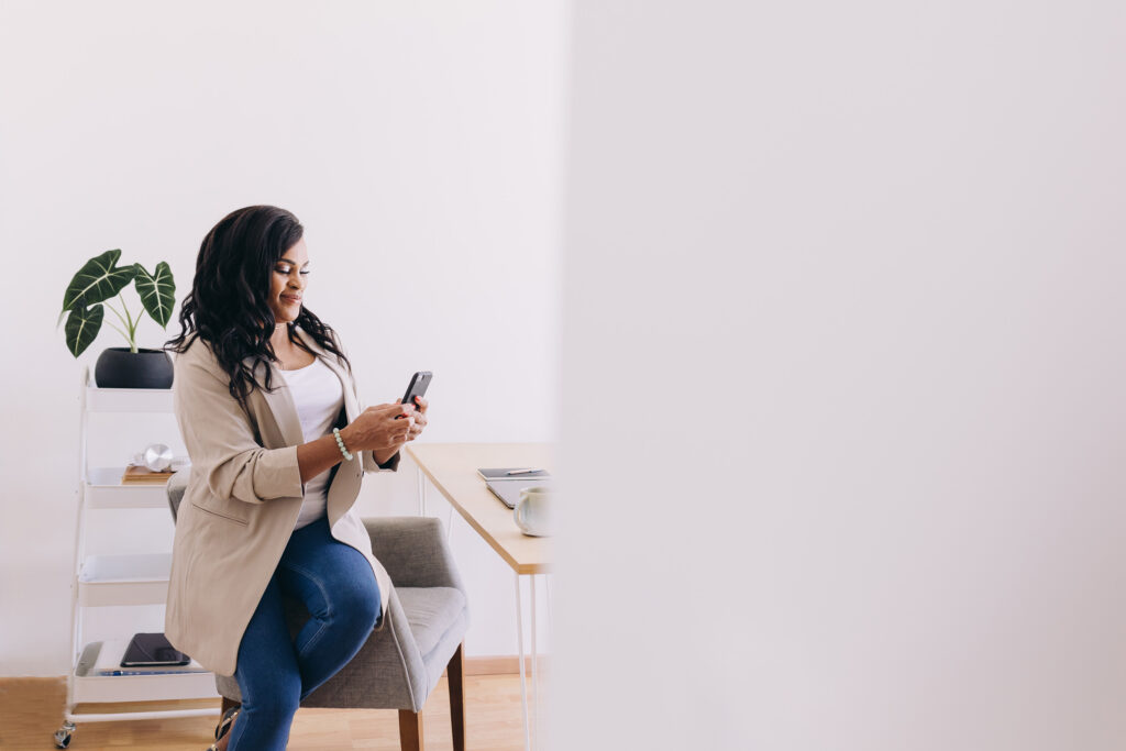 Black woman sitting on desk and looking at her phone
